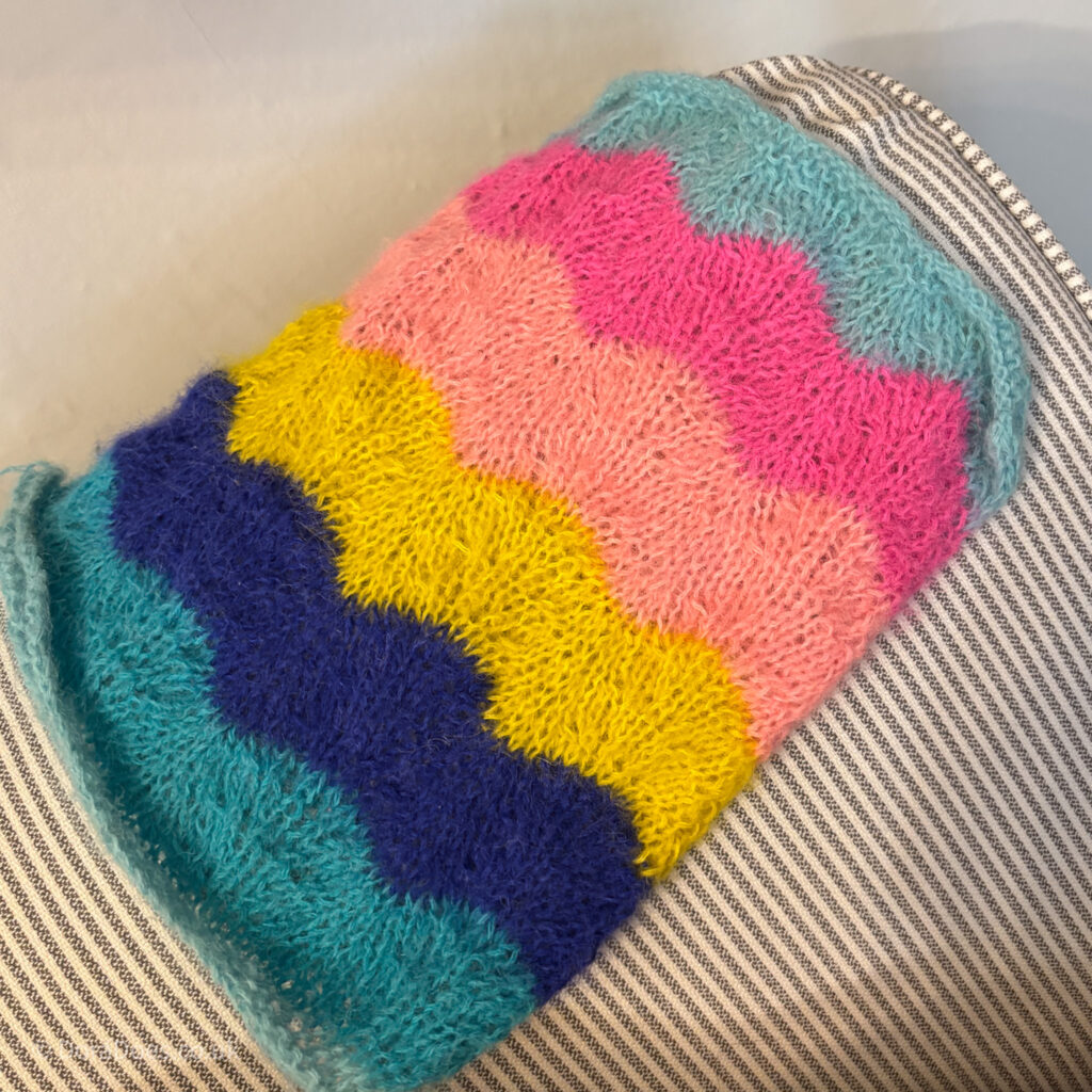 A brightly coloured knitted swatch with a wave pattern in bright coloured pinks, blues and yellow yarn.