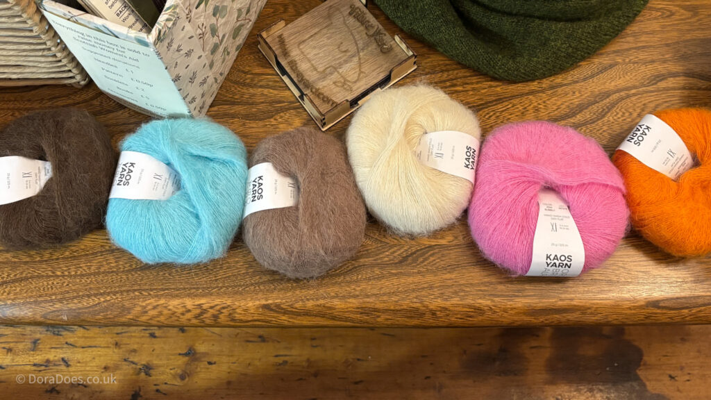Six balls of fluffy brushed alpaca yarn in bright and neutral tones lined up on a wooden table.