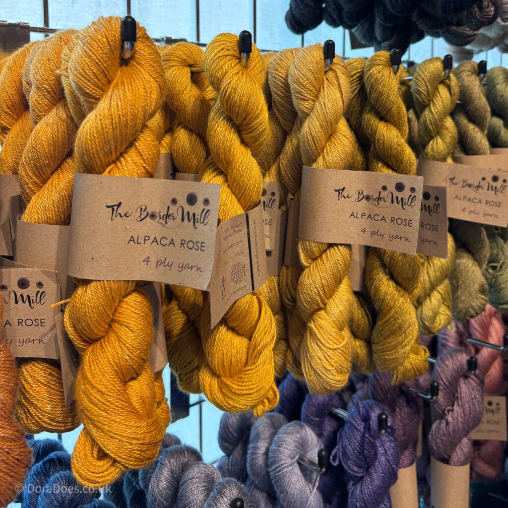 A close up of some shiny yarn in shades of yellow and purple with the maker label reading ‘The Border Mill Alpaca Rose 4 ply yarn.’