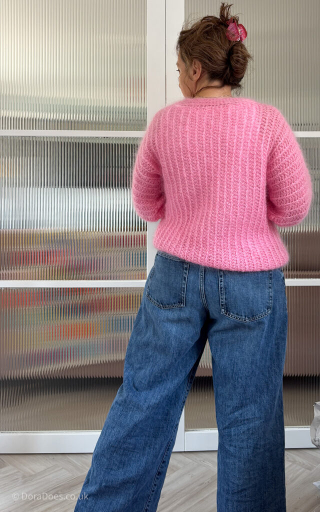 A full length view of Dora from behind wearing the ‘fluff it’ crochet cardigan made with bought pink Kid mohair silk yarn.