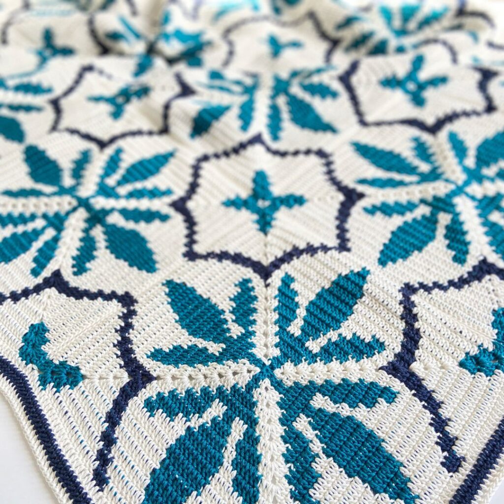 A geometric tapestry crochet blanket with teal retro flower patterns