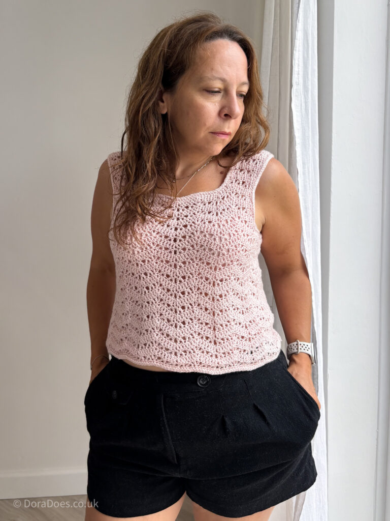Dora stands with hands in pockets wearing a pink chevron vest top paired with black shorts.