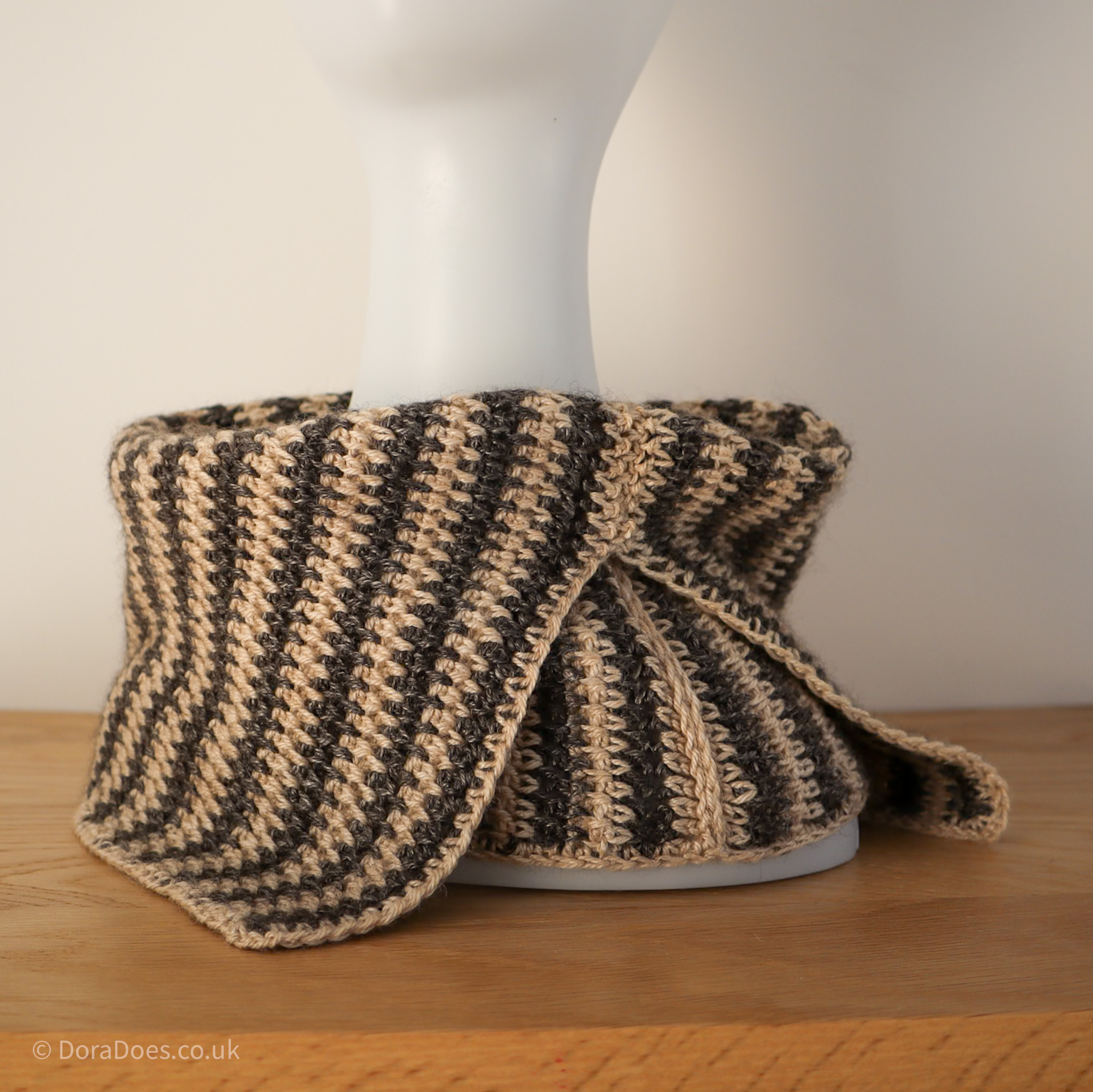 A square image showing one of the ways to wear the ‘between the thorns’ crochet cowl. It is seen folded over with the collar split worn to one side, over the shoulder of the mannequin.