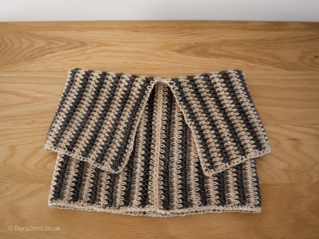 A brown and cream crochet cowl worked in vertical stripes with the top folded over to create a collar.