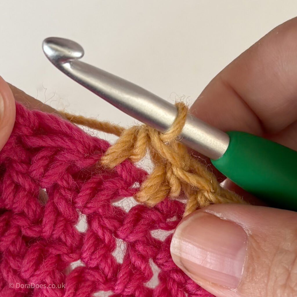 A close up of a half double crochet stitch being crocheted between the posts.
