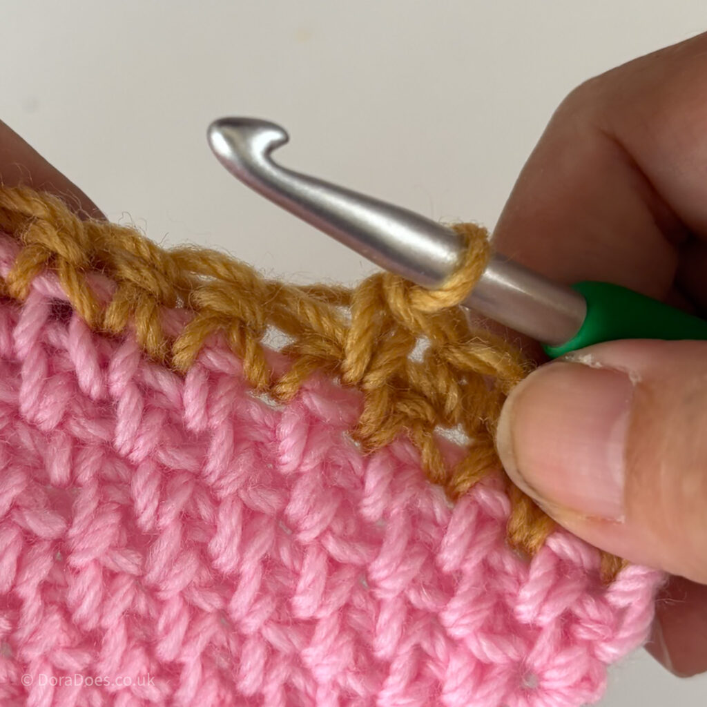 A close up of a single crochet made between the posts in mustard yarn into the top of a pink swatch of the same stitches.